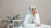 Woman wearing a white hijab sitting on a bed with a neutral background