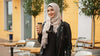 Woman holding a coffee cup outdoors with a building and trees in the background