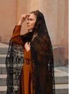 Woman wearing a brown dress and black lace veil standing outdoors.